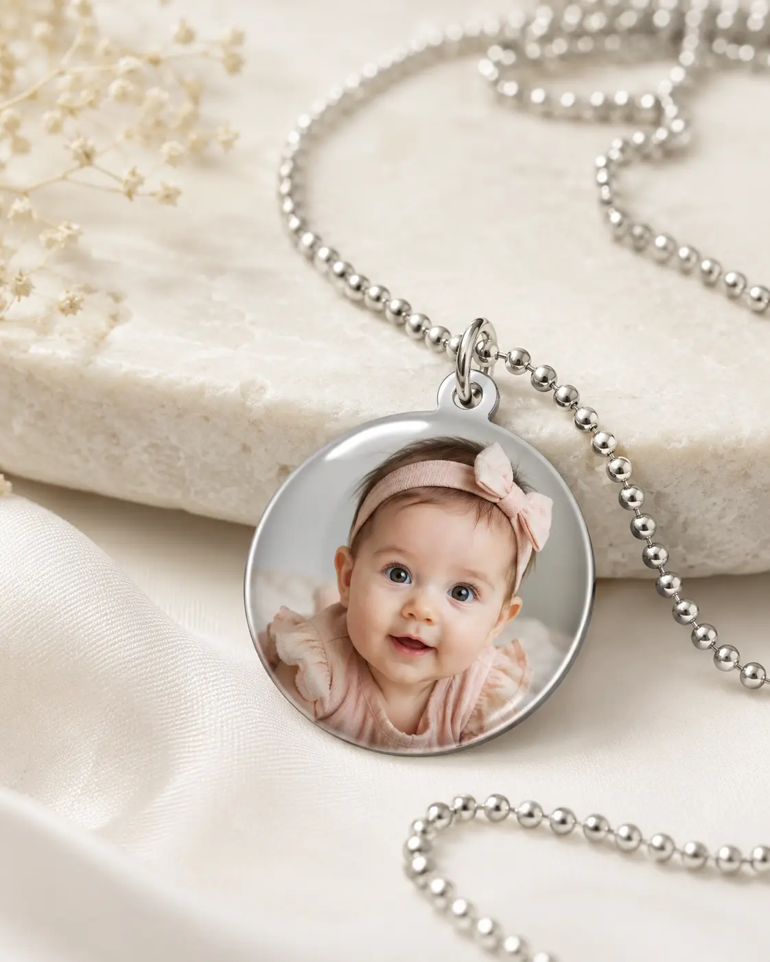 Dije personalizado con fotografía de bebé sobre una tela clara